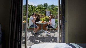 Een kamer met een grote schuifpui die uitkomt op een terras met eettafel en stoelen.