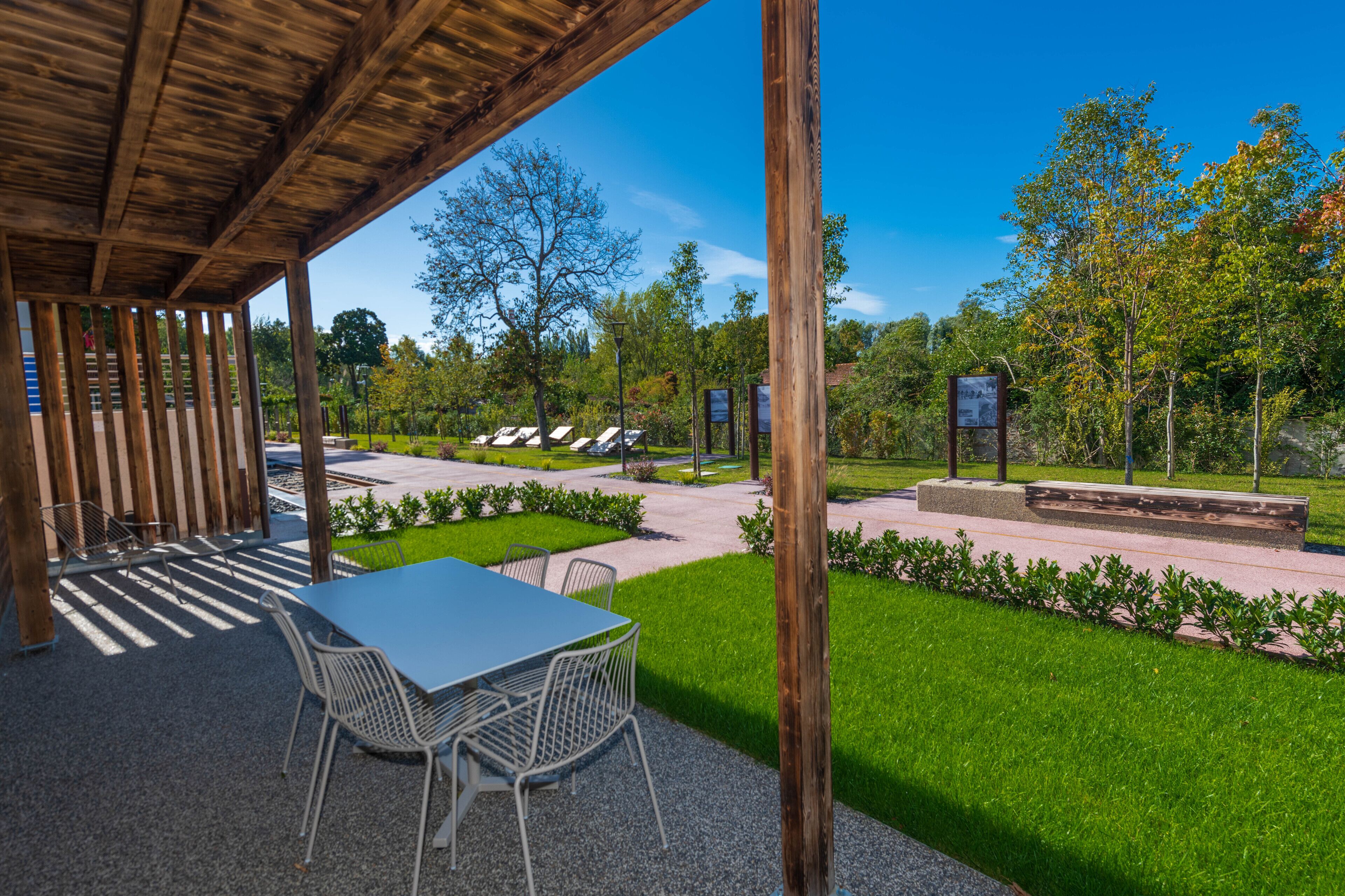 A covered patio area with a table and chairs, surrounded by a well-maintained lawn and trees.