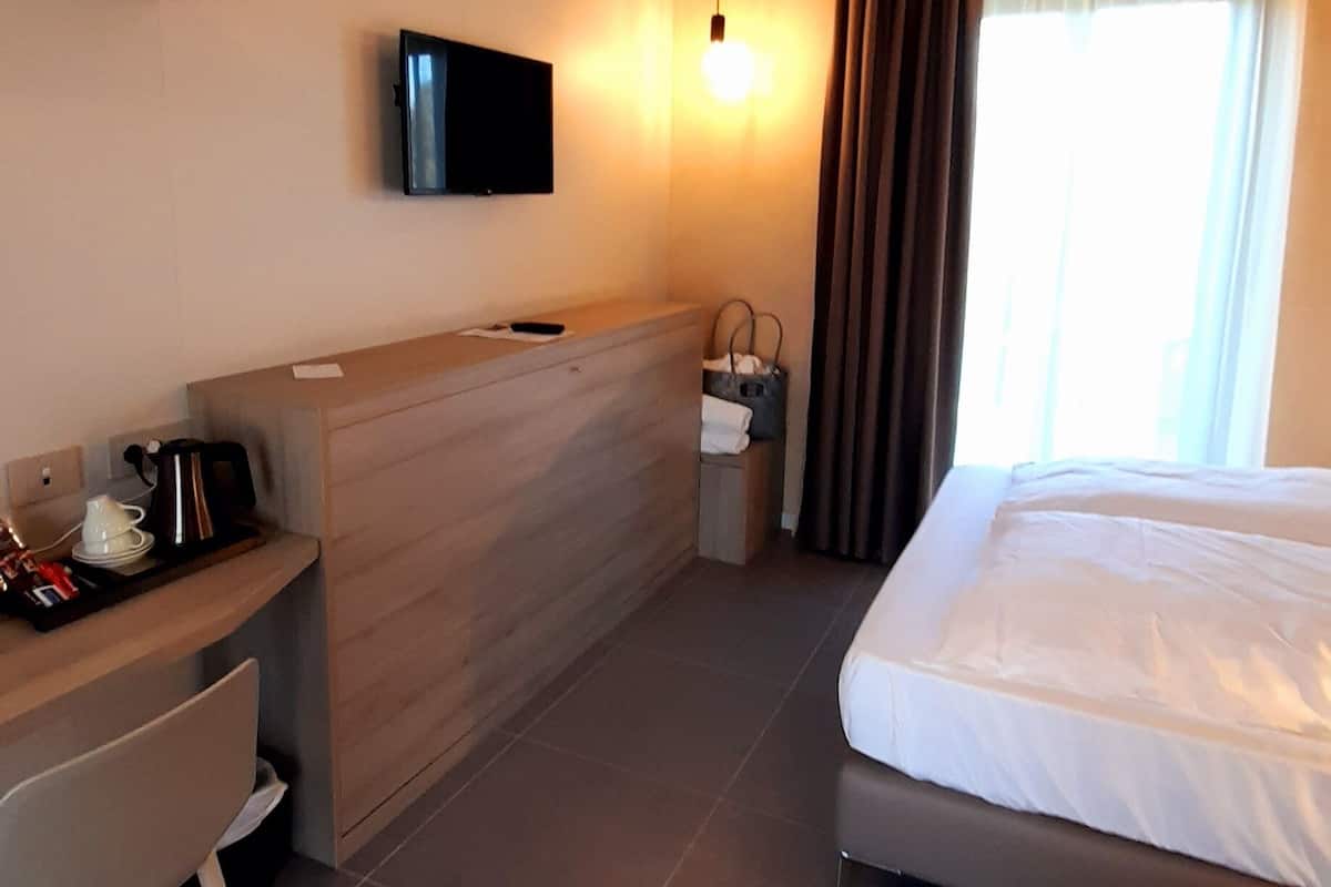 Une chambre d’hôtel avec un lit, un bureau, une télévision et une fenêtre avec des rideaux.