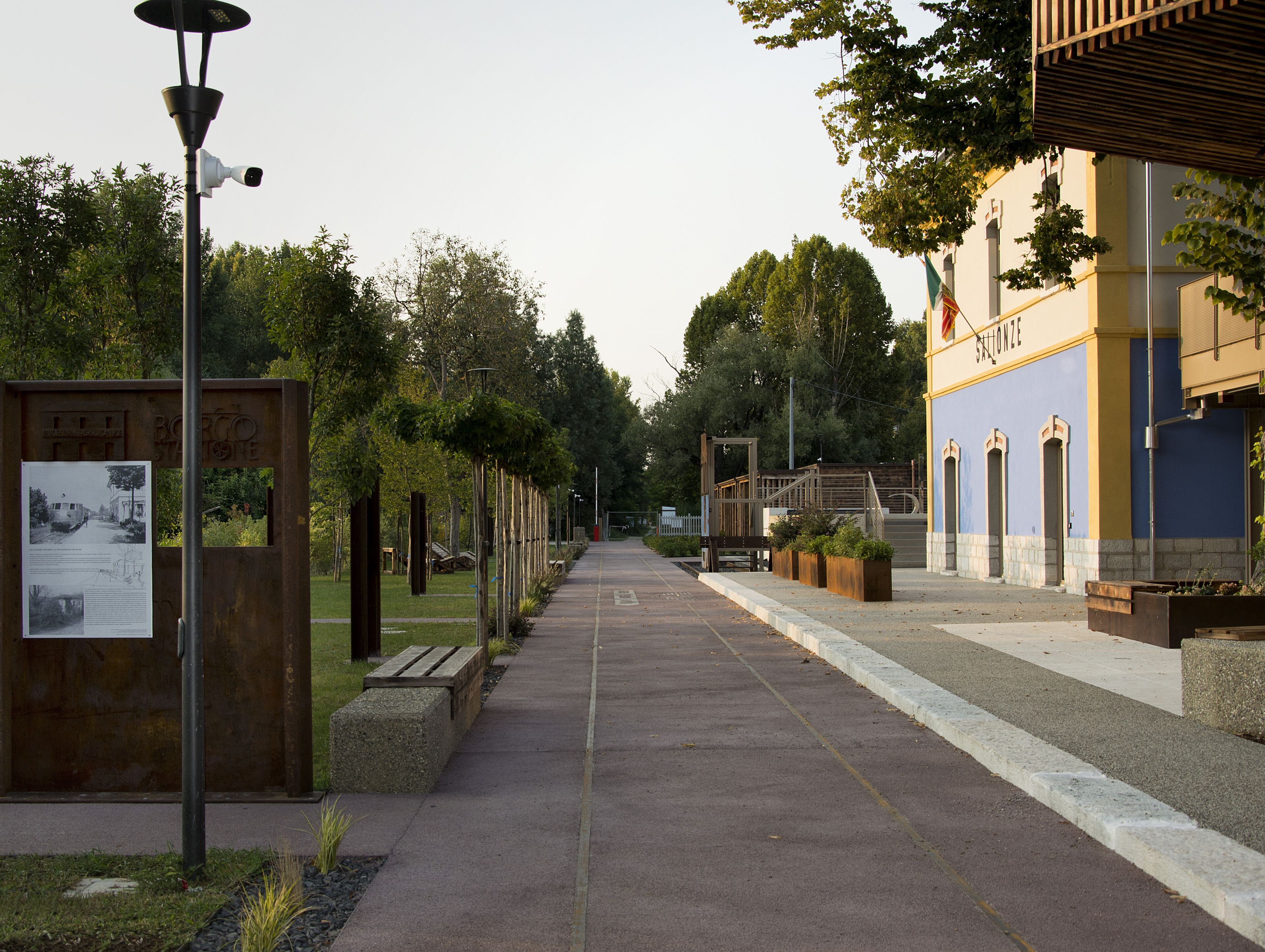 Un sentier bordé de panneaux d’information et de bancs, qui mène à un bâtiment à la façade bleue et aux fenêtres en arc de cercle.