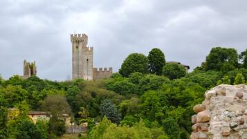 A historic stone tower with battlements, surrounded by lush greenery and a small building with a tiled roof.