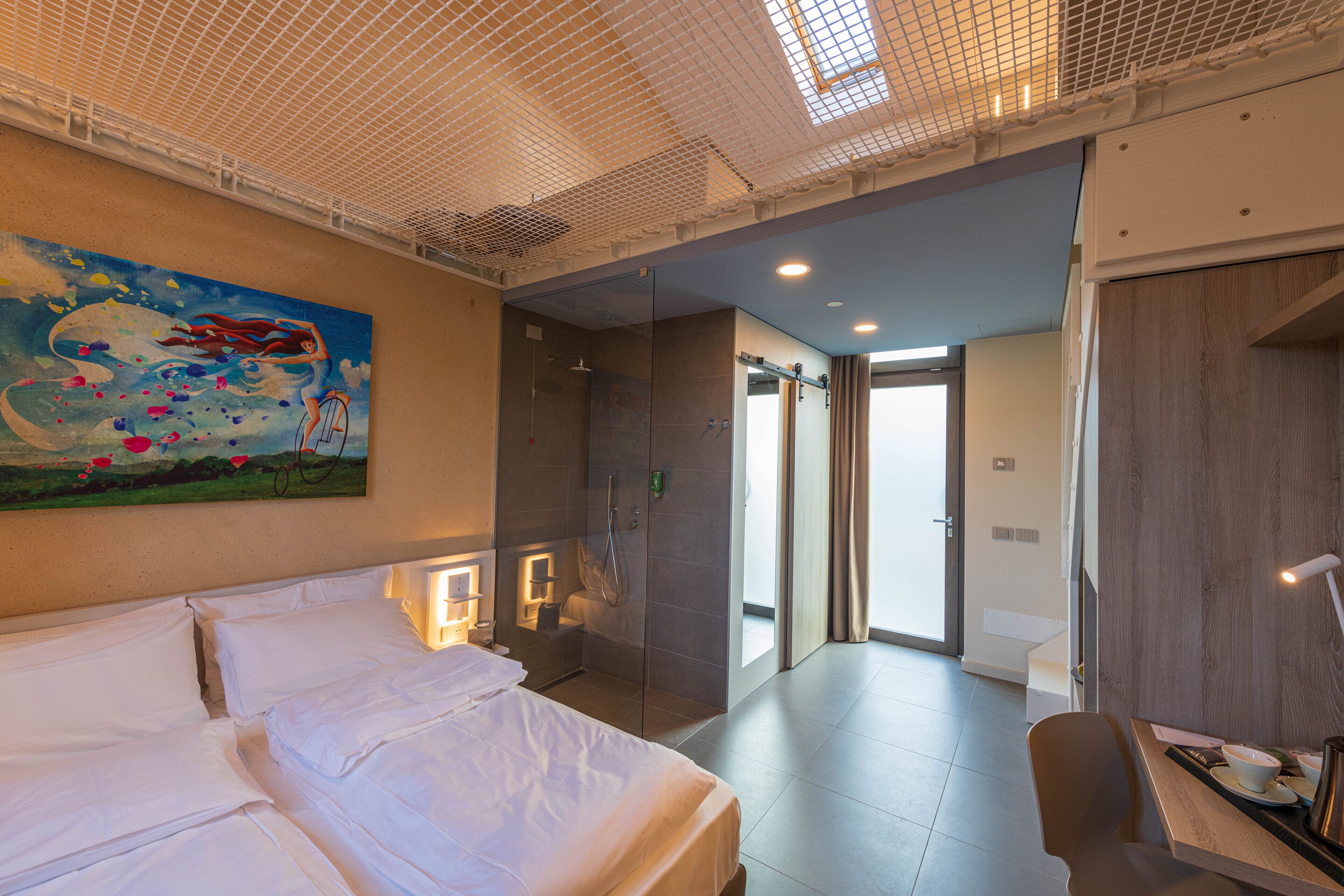 Ein Hotelzimmer mit Bett, Schreibtisch, Dusche und einem Gemälde an der Wand.
