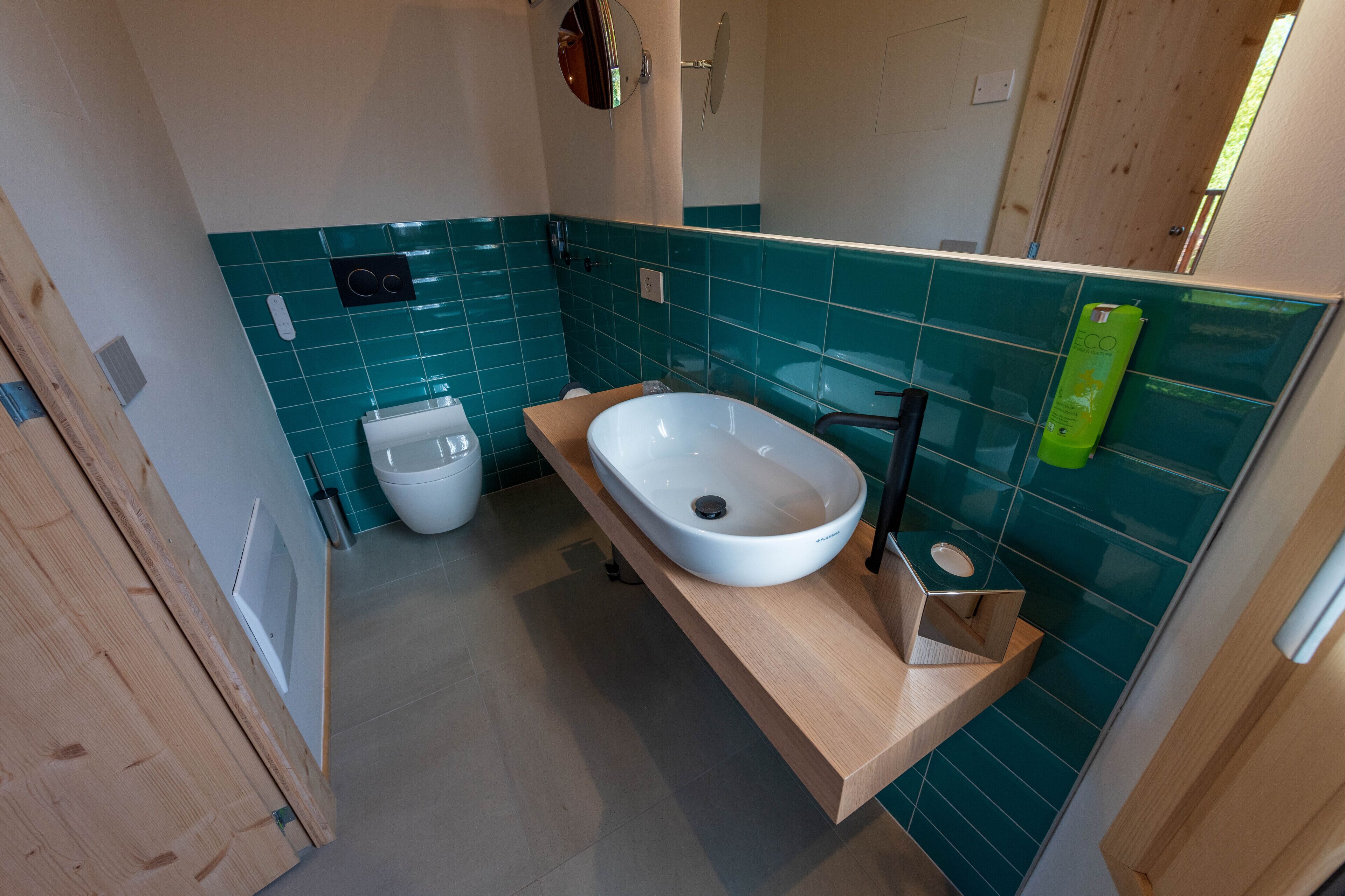 Ein modernes Badezimmer mit weißem Waschbecken, Holzschrank und türkisblauen Fliesen.