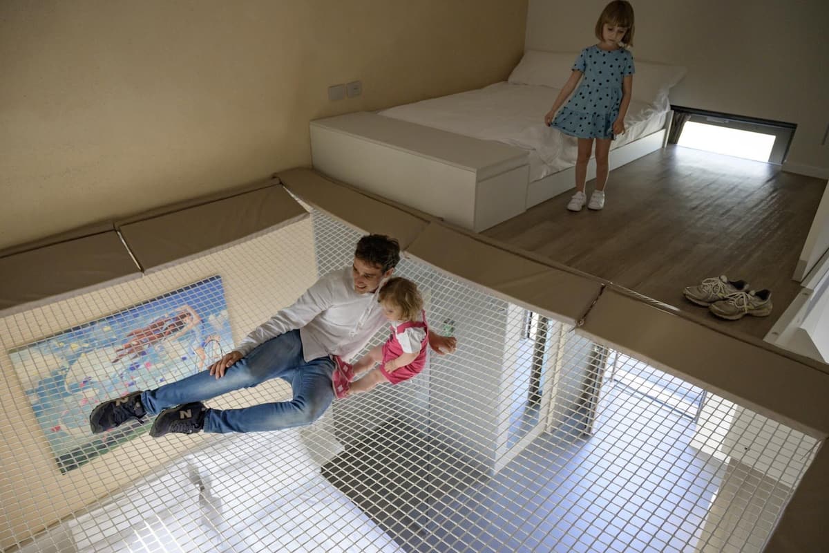 Une chambre avec un lit superposé, une petite fenêtre et un espace de jeu délimité par un filet.