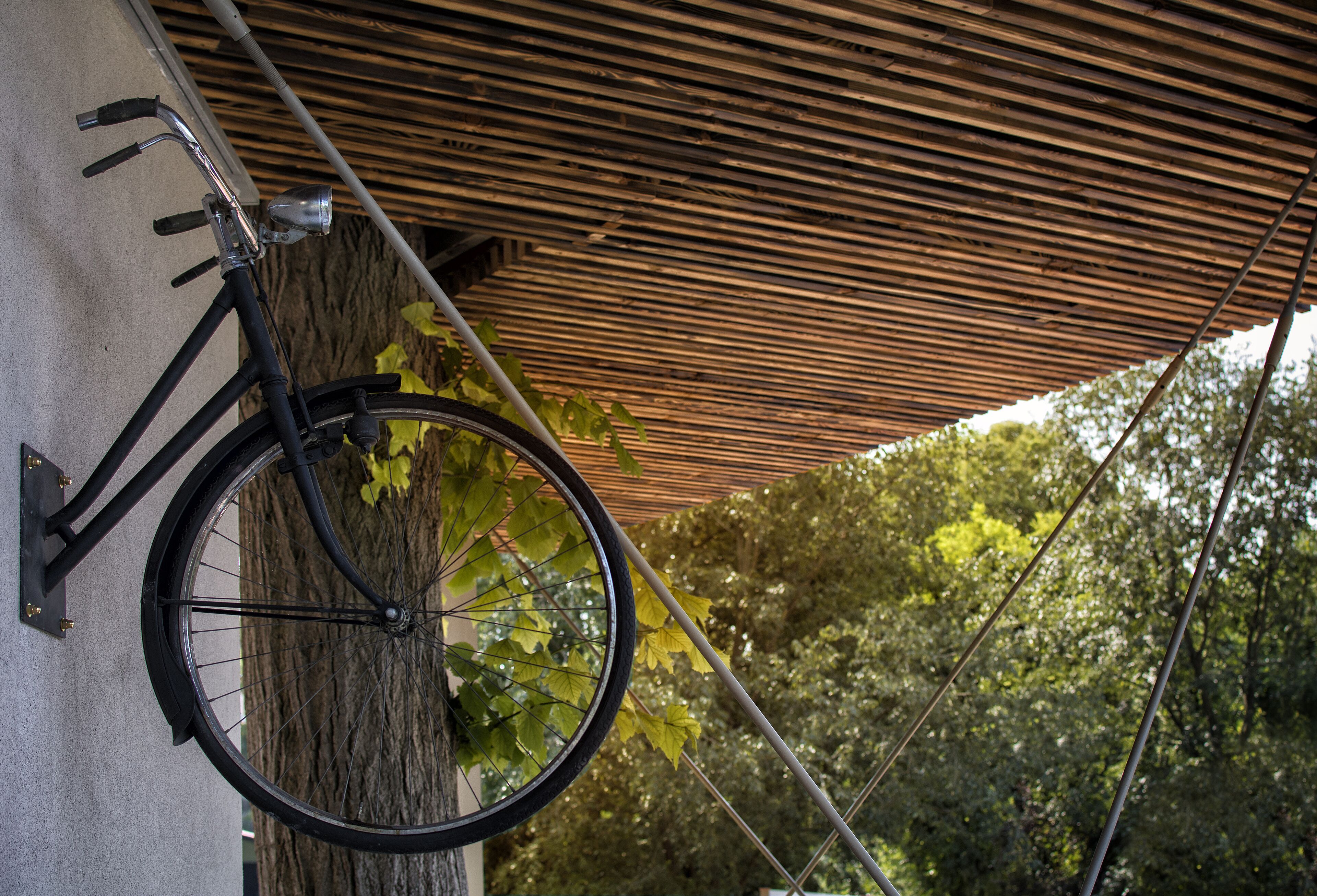 A bicycle leaning against a wall with a wooden slatted roof overhead.