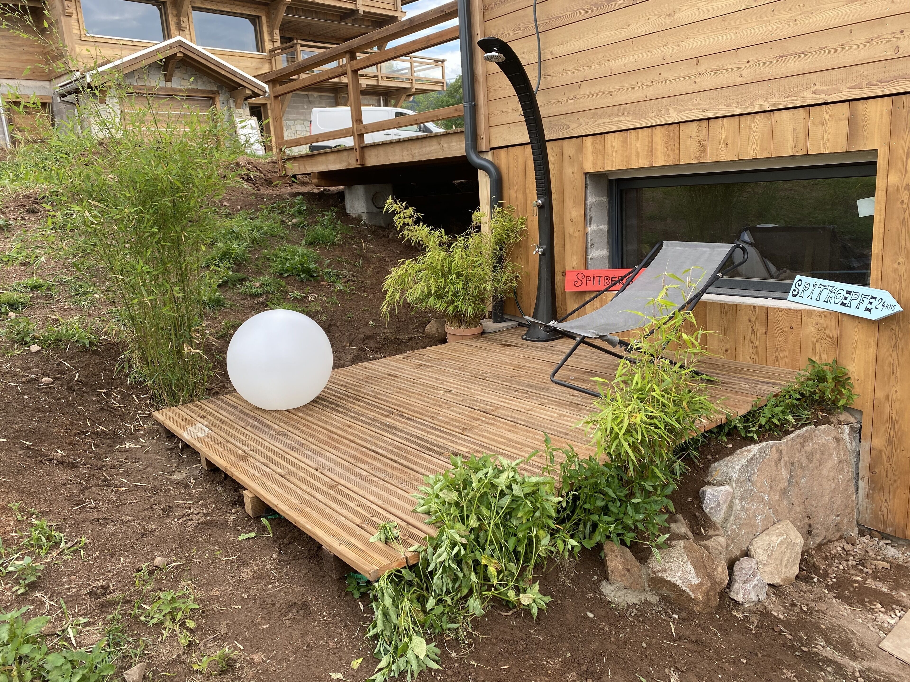 A wooden deck with a lounge chair and a large white balloon, surrounded by greenery and a wooden fence.