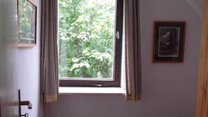 A small, single-bed room with a window, a door with a key, and a framed picture on the wall.