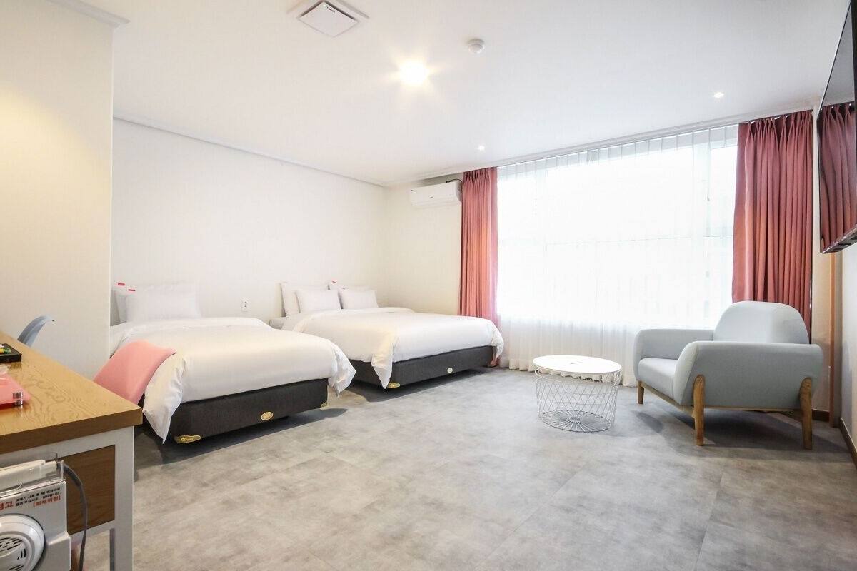 Une chambre d’hôtel avec deux lits, un bureau, une chaise, une télévision et une fenêtre avec des rideaux.