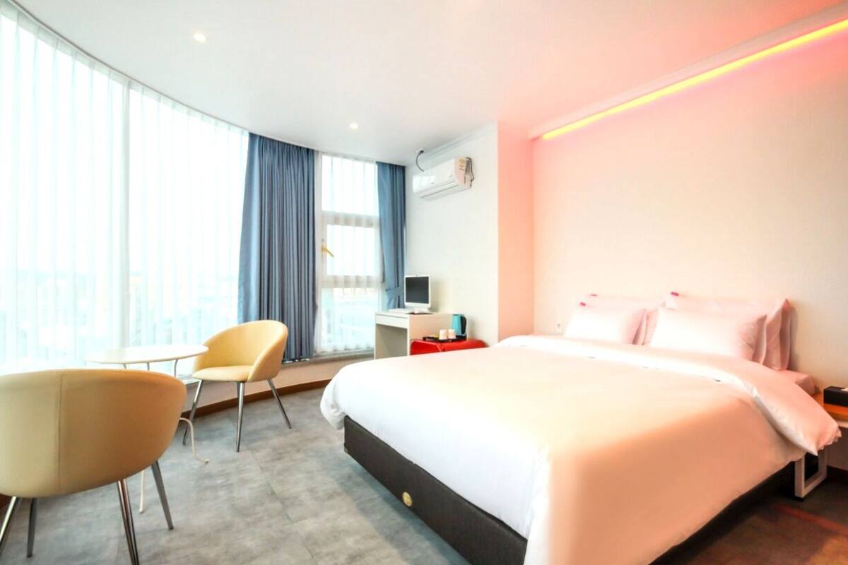 Une chambre d’hôtel avec un grand lit, un bureau, une chaise et une fenêtre avec des rideaux.