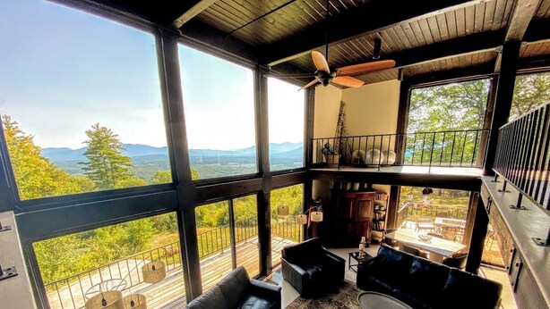 Amplia habitación con grandes ventanales que ofrecen vistas a la montaña, ventilador de techo y una zona de estar acogedora con sofá y mesa de centro.