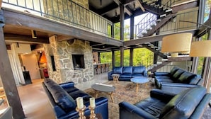 Un espacio interior amplio con chimenea de piedra, varios rincones de estar con sofás y una mesa de centro, y una escalera que conduce a un nivel superior.