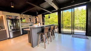 Cocina moderna con una isla central, taburetes de bar y un amplio ventanal con vistas a zonas verdes.