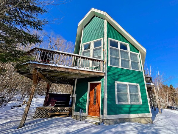 A two-story house with a green exterior, a wooden deck, and a red door.