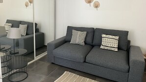 Ein modernes Wohnzimmer mit einem grauen Sofa, gemusterten Kissen, einem kleinen runden Tisch und einer Stehlampe.