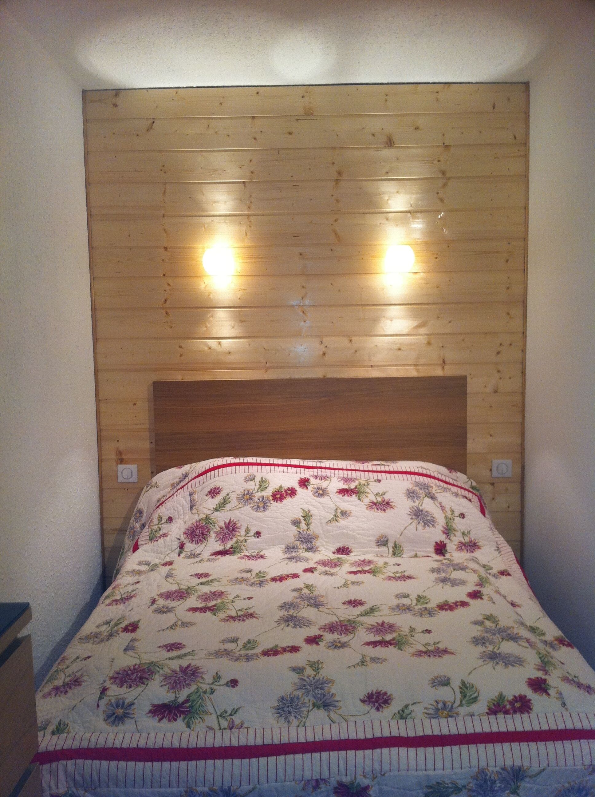Ein Schlafzimmer mit einem Holz-Kopfteil, floralem Bettbezug und zwei Wandleuchten.