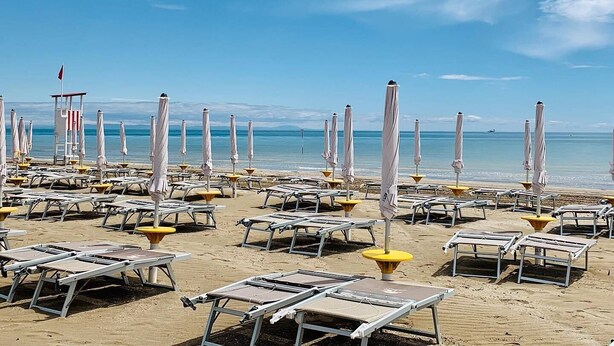 A beach with sun loungers and umbrellas, a lifeguard tower, and the ocean in the background.