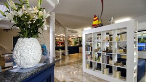 A hotel lobby with a marble floor, a white decorative pineapple centerpiece, a bookshelf with various items, and a small sailboat model on top.