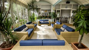 A sunlit indoor seating area with wicker furniture and potted plants.