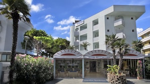 A hotel with a modern facade, multiple balconies, and a covered entrance area with seating.