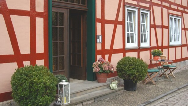A traditional half-timbered building with a green door, potted plants, and outdoor seating. - House Froschkönig directly on the Weser (Hann. Münden)