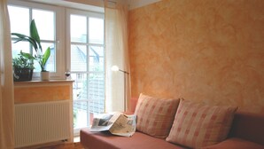 A cozy room with a red sofa, a window with curtains, a radiator, and a plant on the windowsill. - House Froschkönig directly on the Weser (Hann. Münden)
