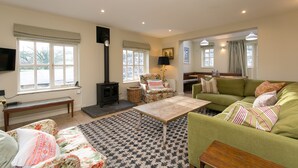 A cozy living room with a sofa, a coffee table, a fireplace, and a television. - Stunning 3-bed House in a Private Hidden Valley (Denbigh)