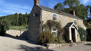 A stone house with a chimney, a satellite dish, and a gravel driveway. - Stunning 3-bed House in a Private Hidden Valley (Denbigh)