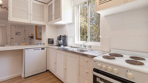 Een compacte keuken met een vaatwasser, een koffiezetapparaat, een spoelbak en een kookplaat.