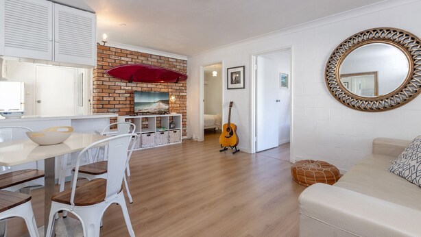 Een moderne woonkamer met een houten vloer, witte meubels, een rode haard en een gitaar.
