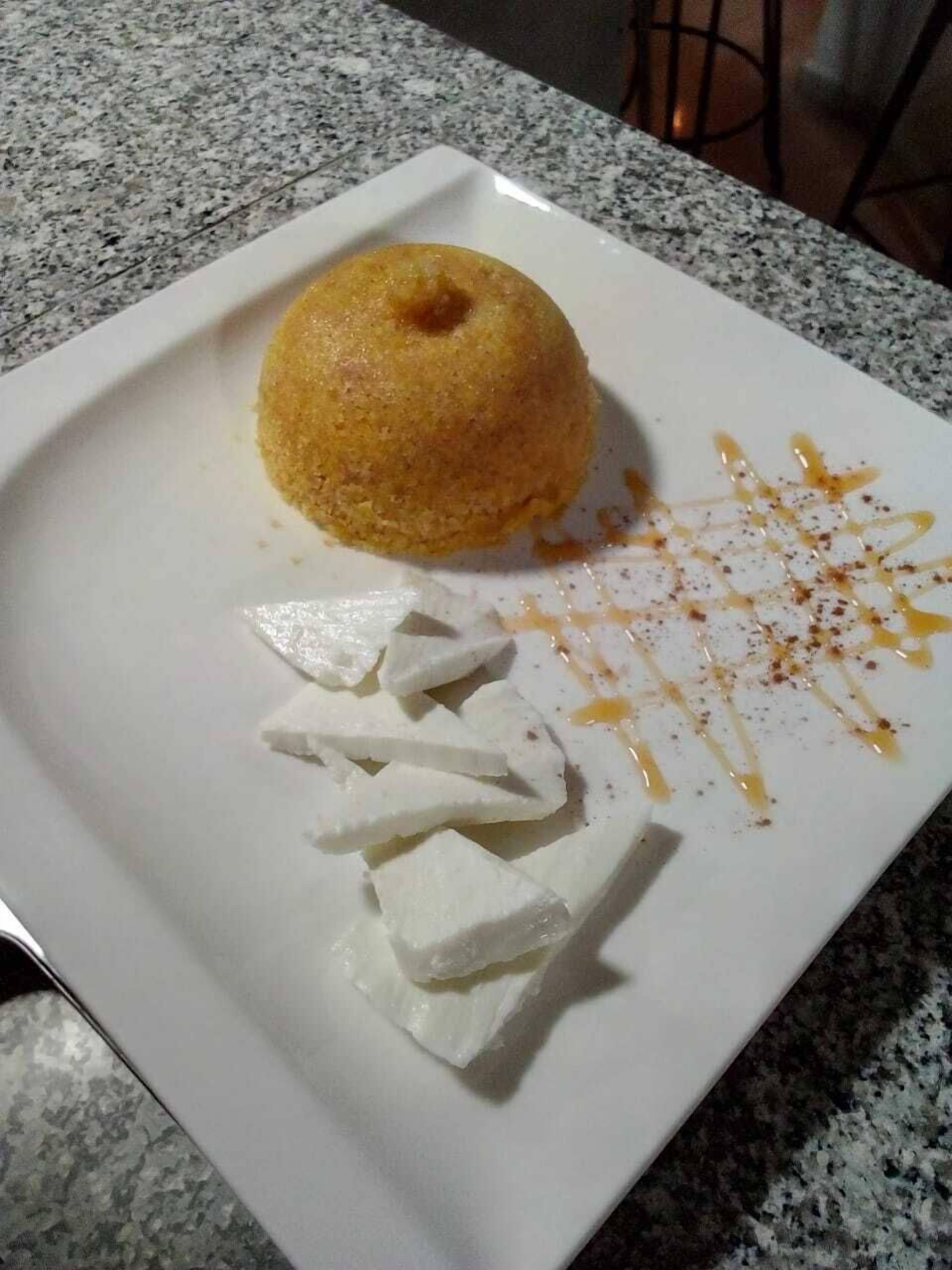 Une assiette à dessert avec un mets de couleur brun doré, peut-être un gâteau, et des cubes blancs, peut-être du fromage, sur une assiette blanche.
