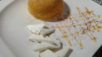 Une assiette à dessert avec un mets de couleur brun doré, peut-être un gâteau, et des cubes blancs, peut-être du fromage, sur une assiette blanche.
