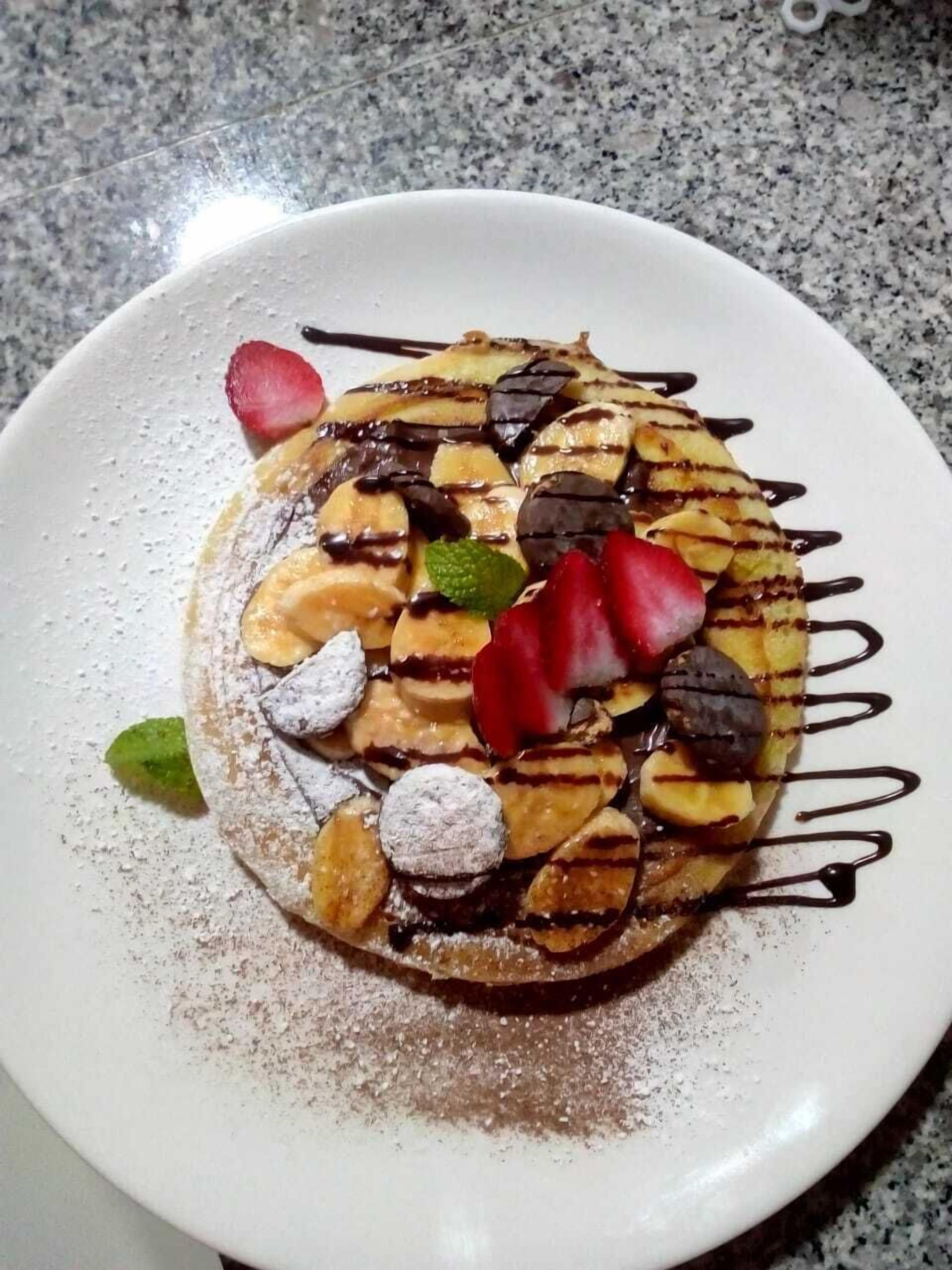 Un dessert servi dans une assiette, nappé de chocolat, agrémenté de fraises et saupoudré de sucre glace.