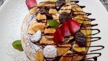 Un dessert servi dans une assiette, nappé de chocolat, agrémenté de fraises et saupoudré de sucre glace.