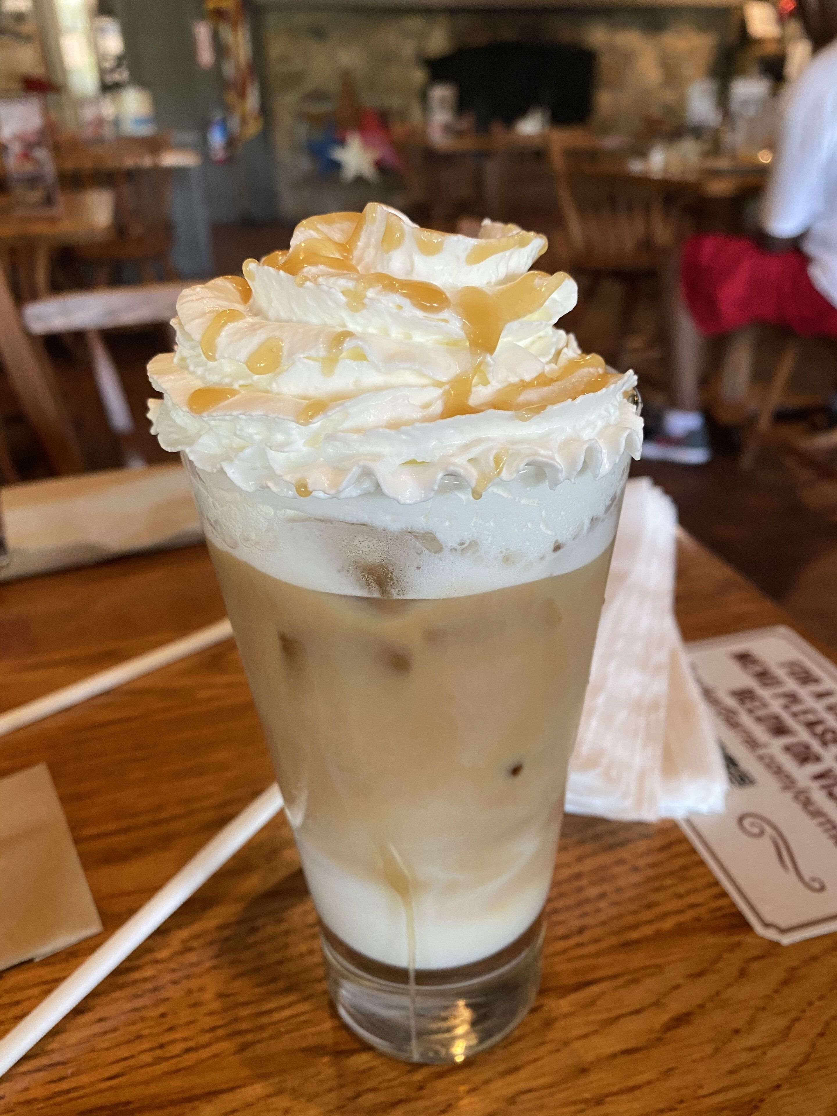A tall glass of iced coffee with whipped cream on top, placed on a wooden table.