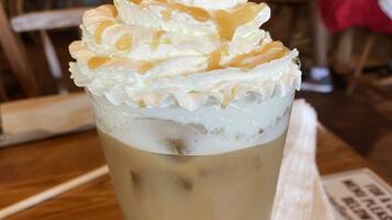 A tall glass of iced coffee with whipped cream on top, placed on a wooden table.
