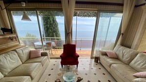 A spacious living room with two beige sofas, a red armchair, and a glass coffee table. Large windows offer a view of the outdoors. - Provenc  beach house, breathtaking sea views pool , 5mn walk to beach  (Ensues la redonne)