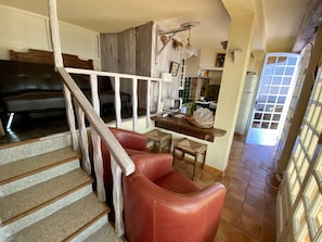 Una escalera con barandilla de madera que lleva a un área de estar con un sofá de cuero rojo y una mesa de madera.