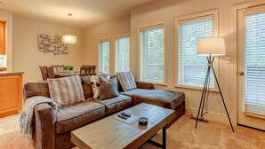 Ein Wohnzimmer mit Sofa, Couchtisch und Stehlampe. Drei Fenster mit Jalousien, eine Wandleuchte und ein dekoratives Wandbild.