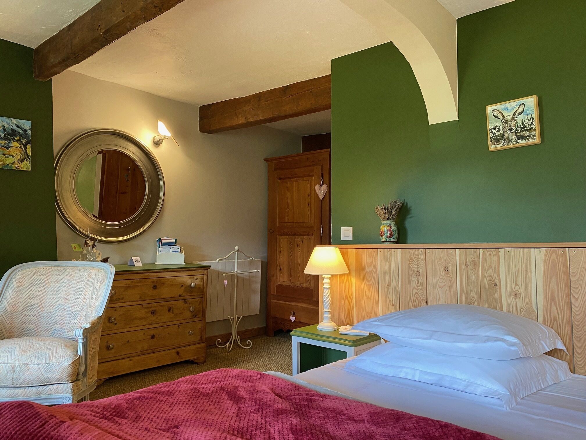 A bedroom with a wooden headboard, a bedside lamp, a dresser, a mirror, and a bed with white linens.
