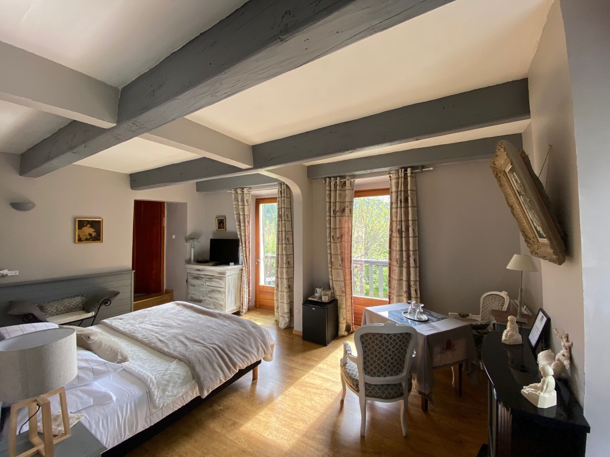 Een slaapkamer met een bed, een bureau en een stoel. Er is een raam met gordijnen, een foto aan de muur en een tv op een dressoir.
