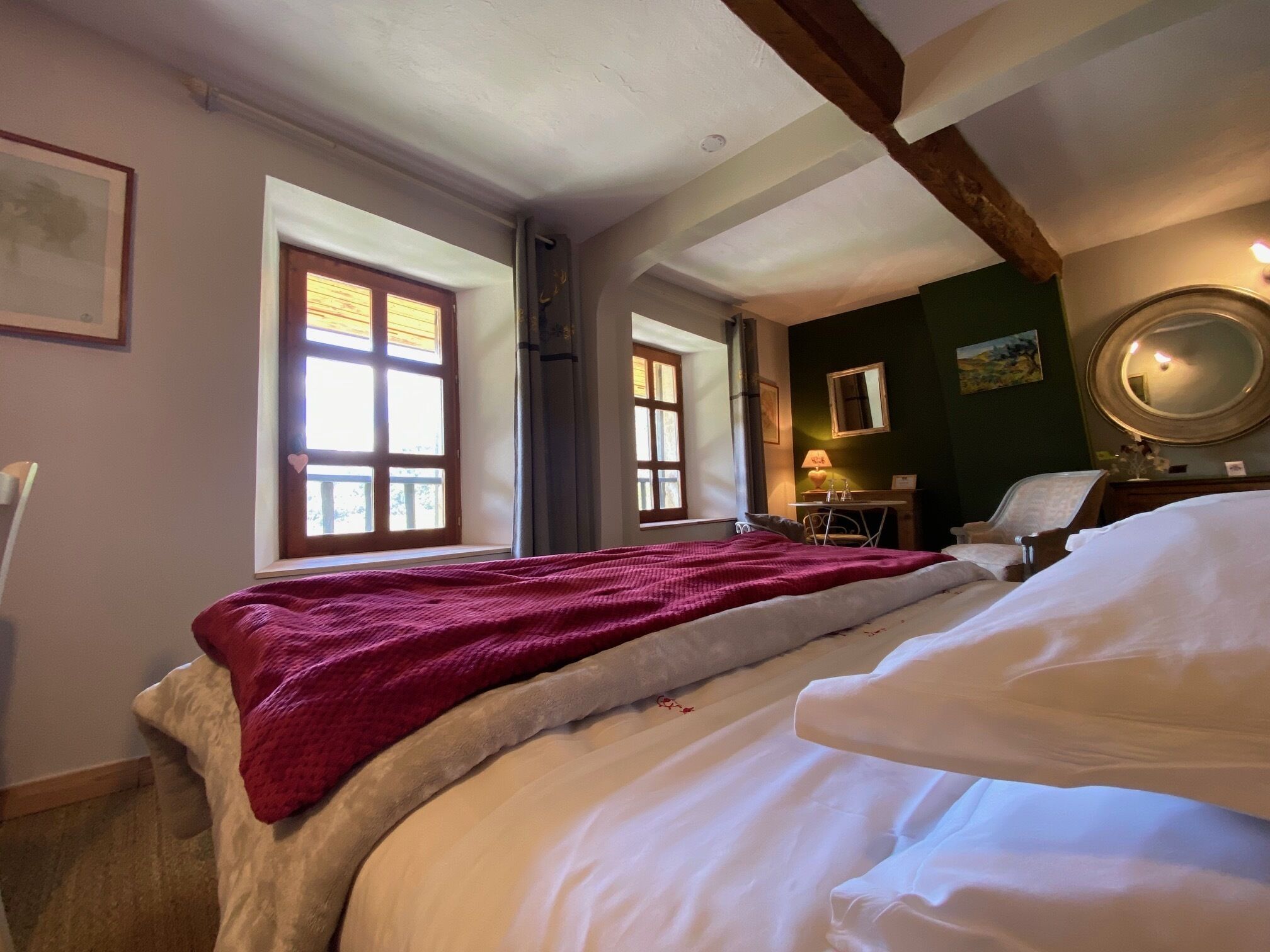 A bedroom with a large bed, a desk, a chair, and a window with curtains.