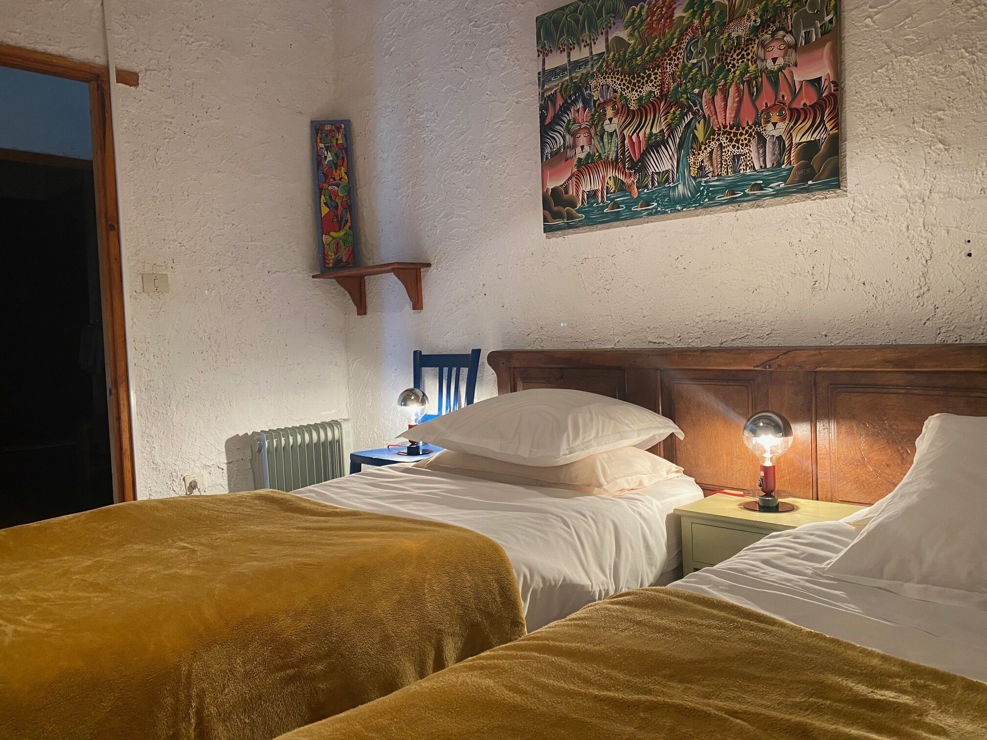 A bedroom with two beds, a nightstand with a lamp, a radiator, and a wall painting.