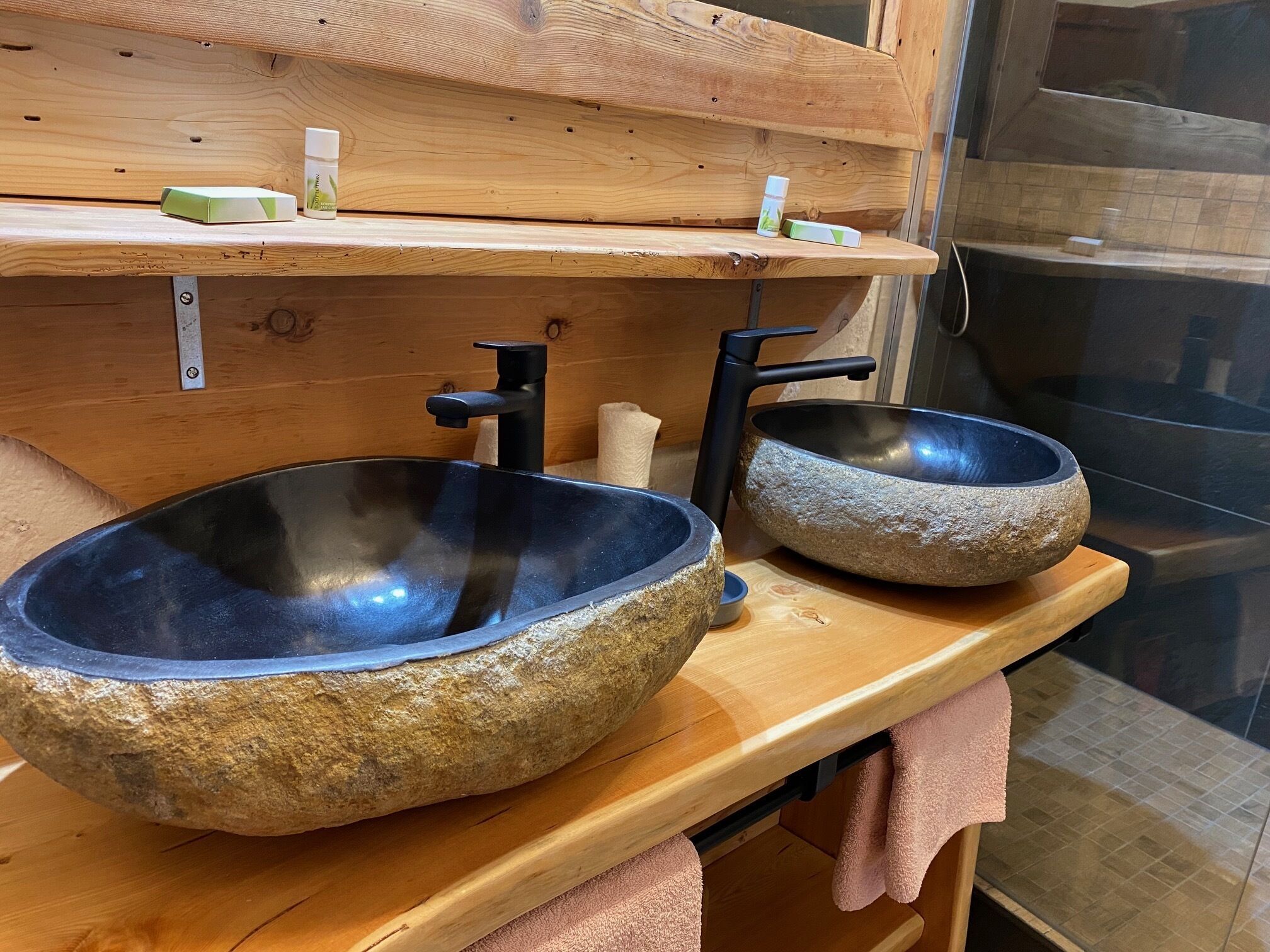 Un baño con dos lavamanos de piedra, estantes de madera y un perchero para toallas.