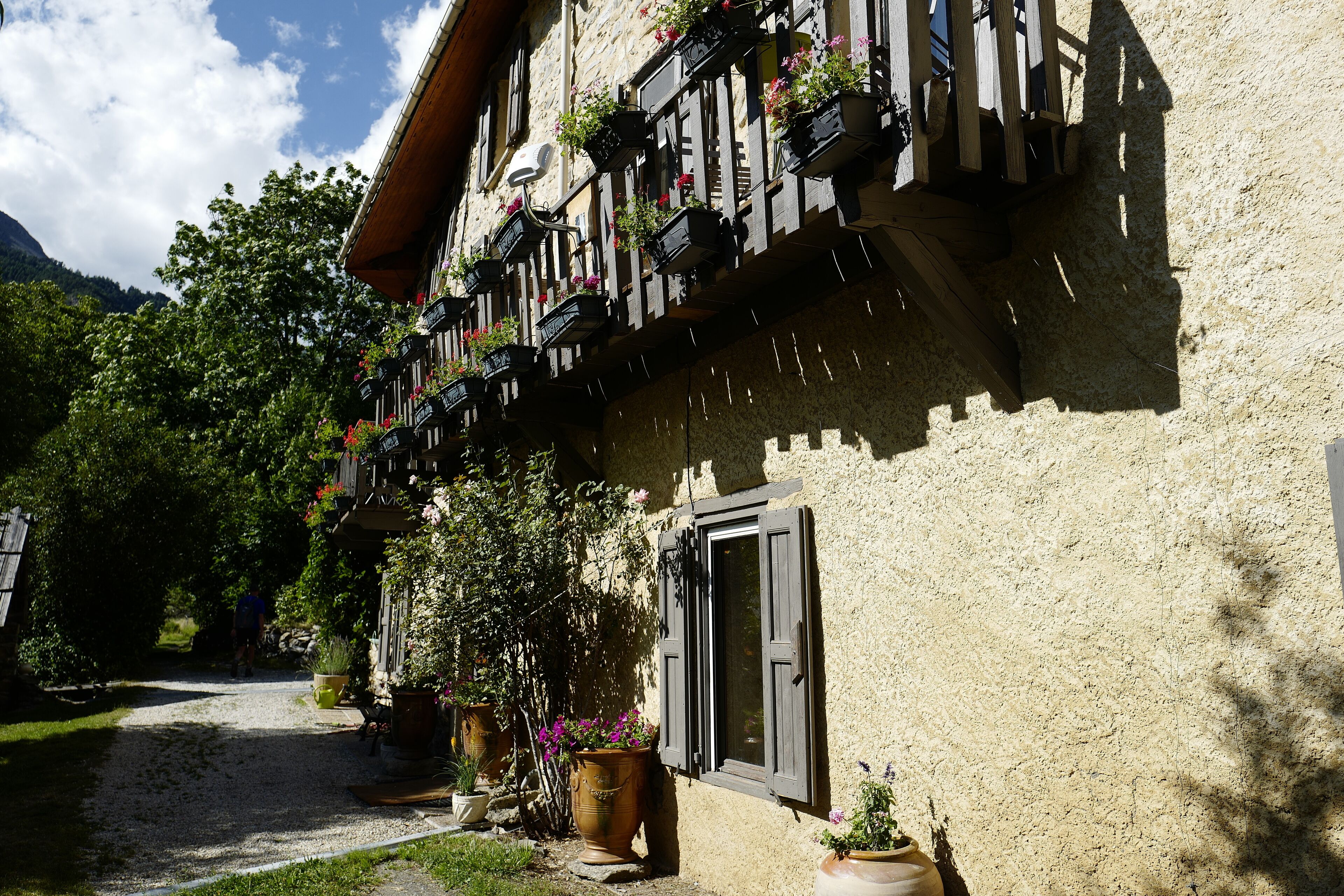 Un edificio con fachada rústica, varios balcones con jardineras y un camino de grava que conduce a la entrada.