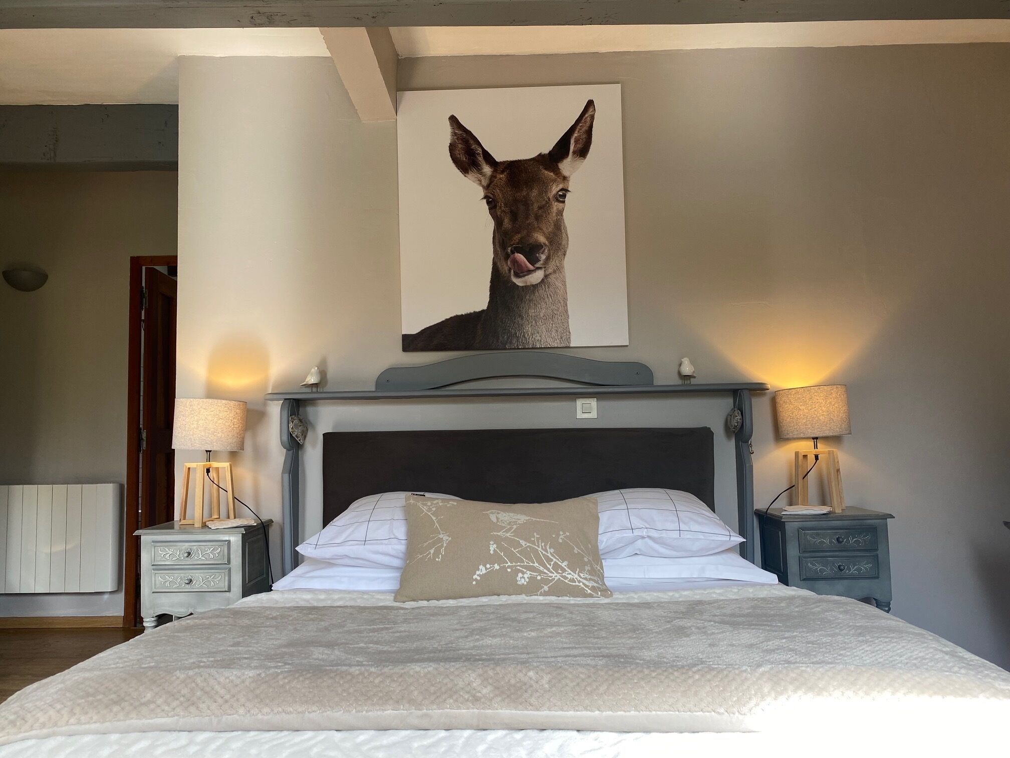 A bedroom with a bed, two bedside tables, a wall-mounted lamp, and a framed picture above the bed.
