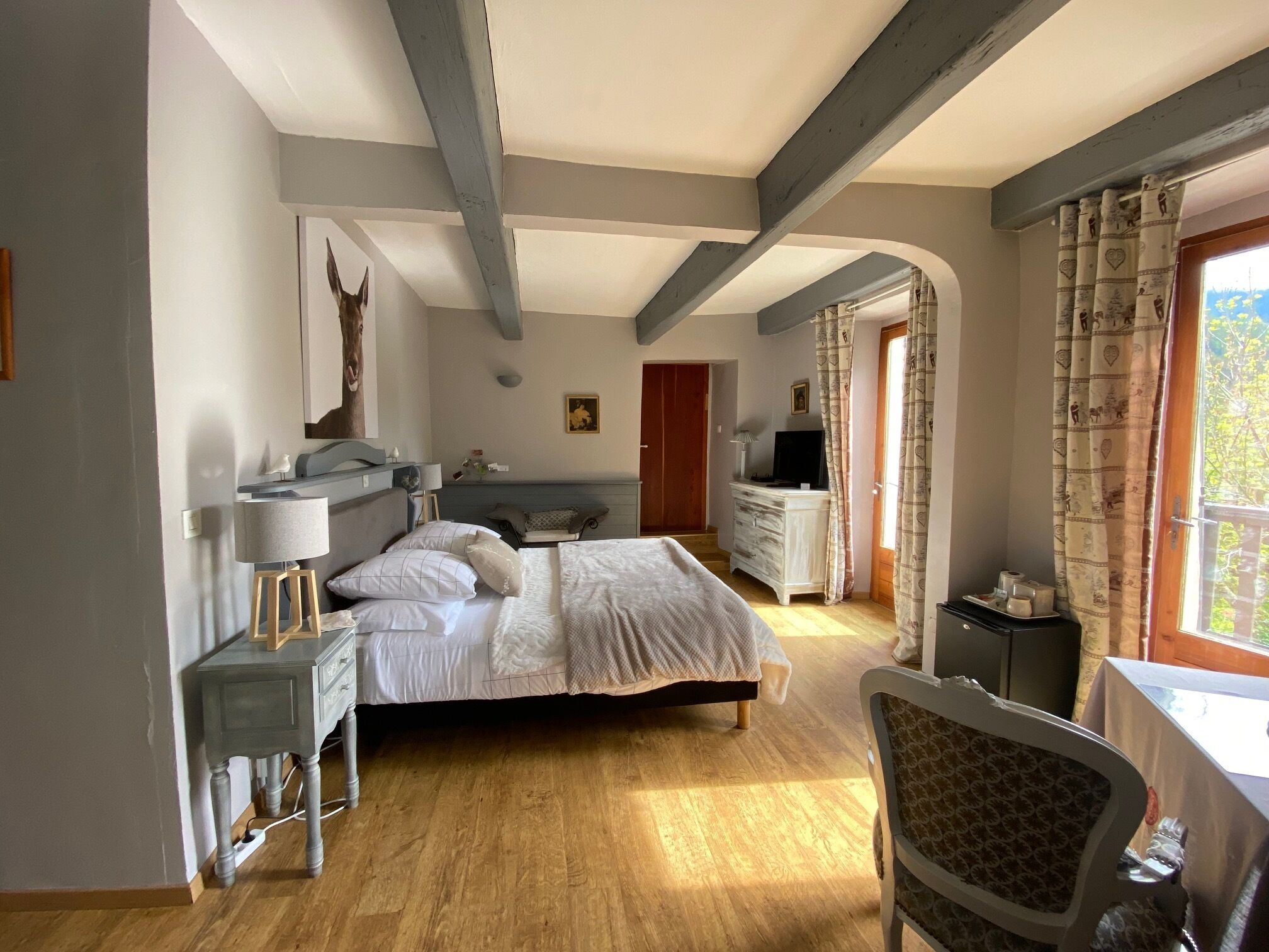 A bedroom with a bed, bedside table, lamp, dresser, and a TV.