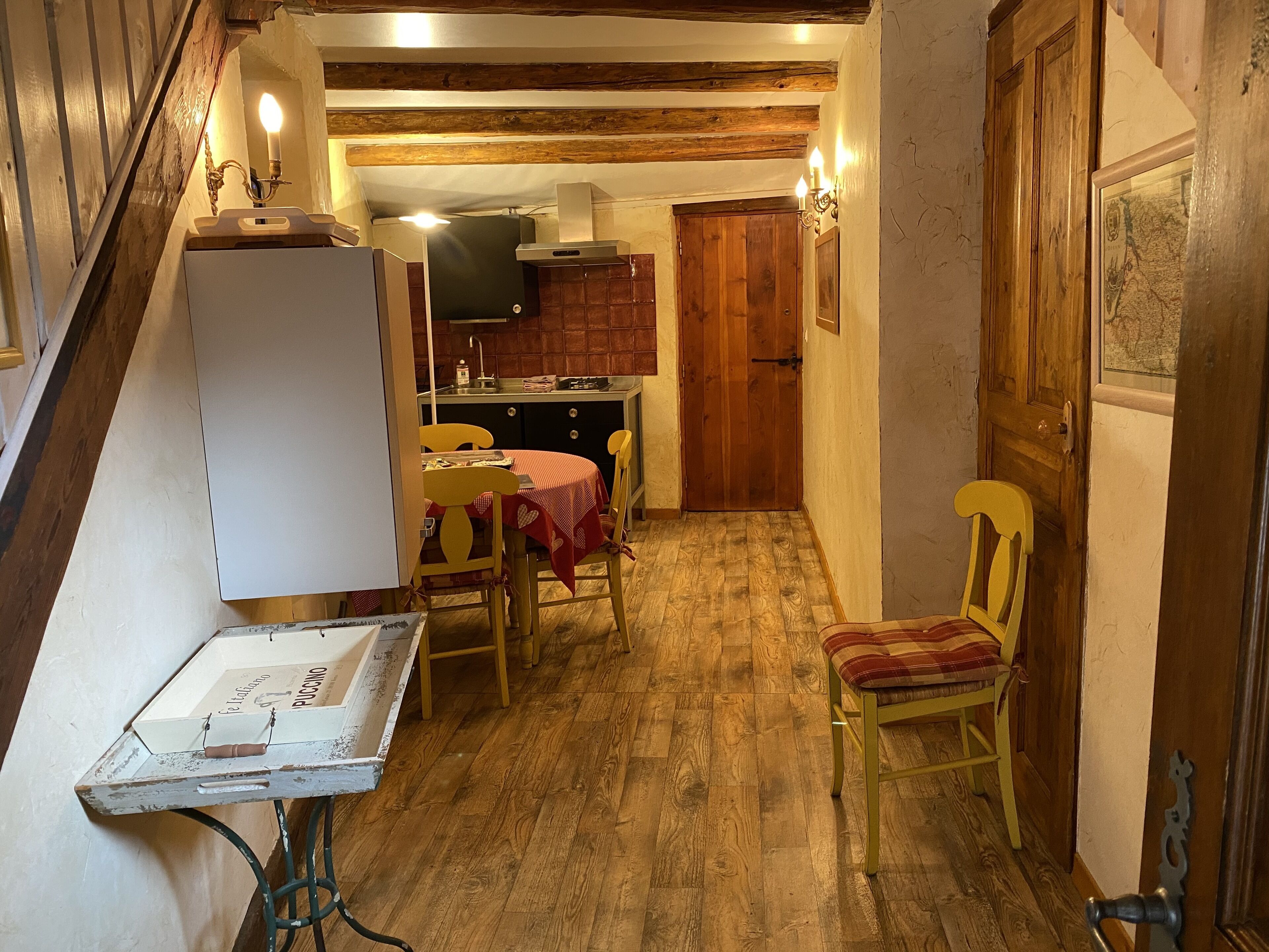 A narrow kitchen with wooden beams, a refrigerator, a stove, and a dining table with chairs.