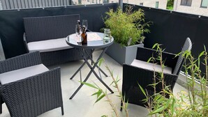 A balcony with wicker furniture, a table with drinks, and a potted plant.