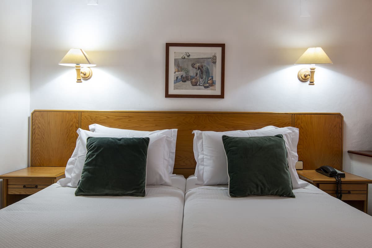 Uma cama de casal com duas almofadas verdes, uma cabeceira de madeira e duas mesas de cabeceira com abajures e um quadro na parede.