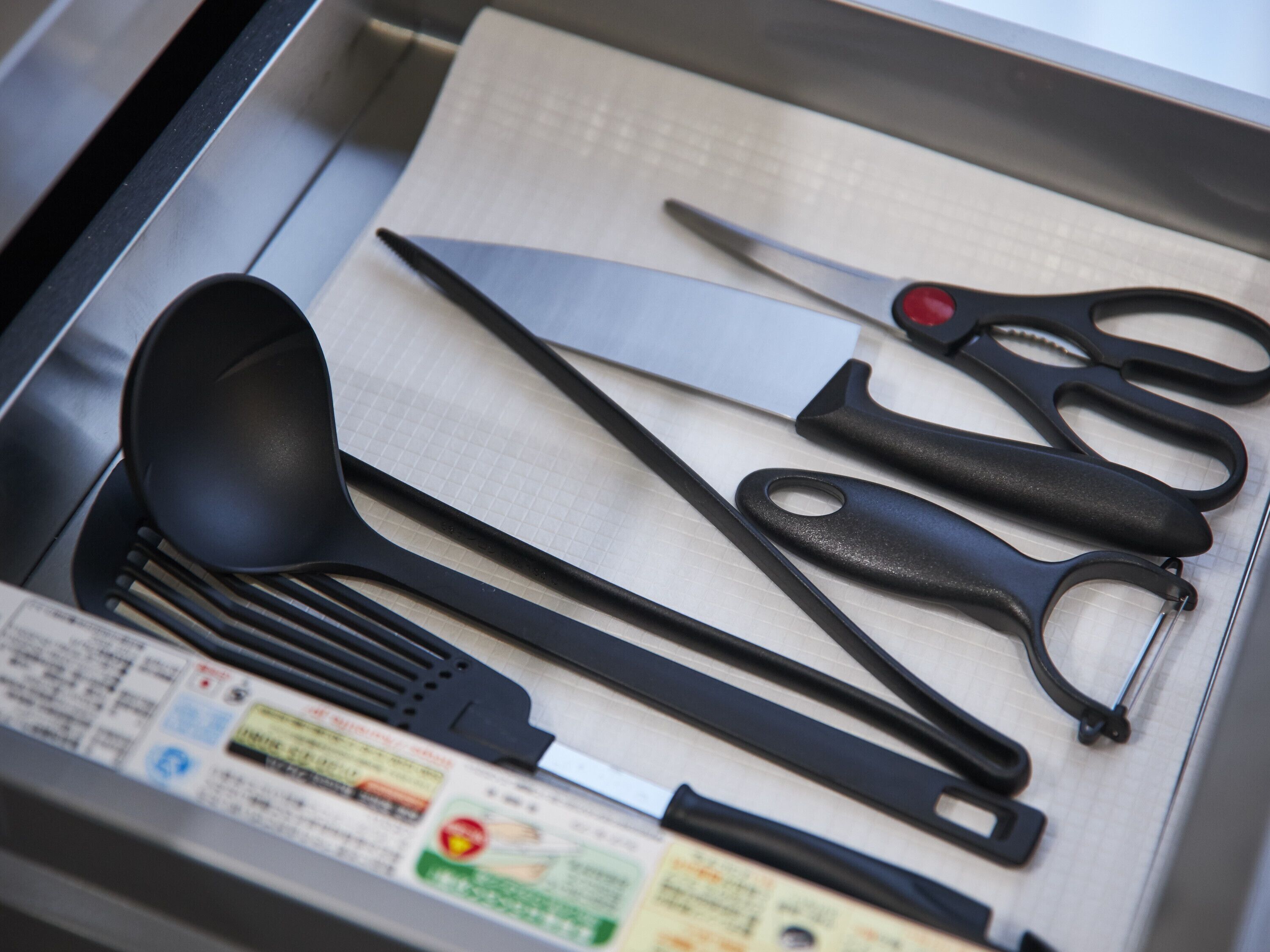 Un cajón con utensilios de cocina, como una espátula, un cuchillo grande y un par de tijeras.